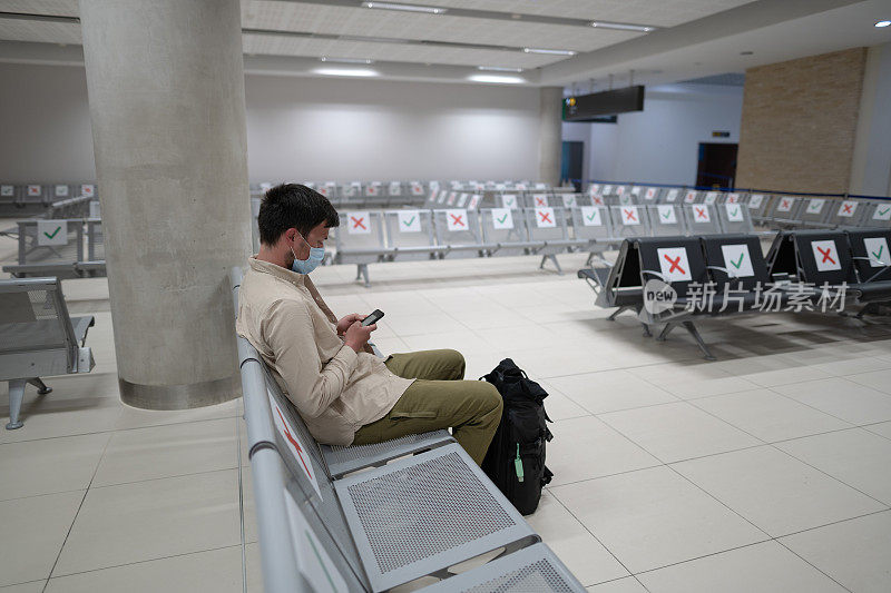 一名戴着防护口罩的男子因航班取消而心烦意乱，他坐在塞浦路斯帕福斯市机场的空航站楼给家人写信，原因是Covid - 19疫情大流行